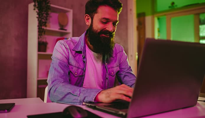 Smiling Man Highlighted by Purple Light and Using Laptop