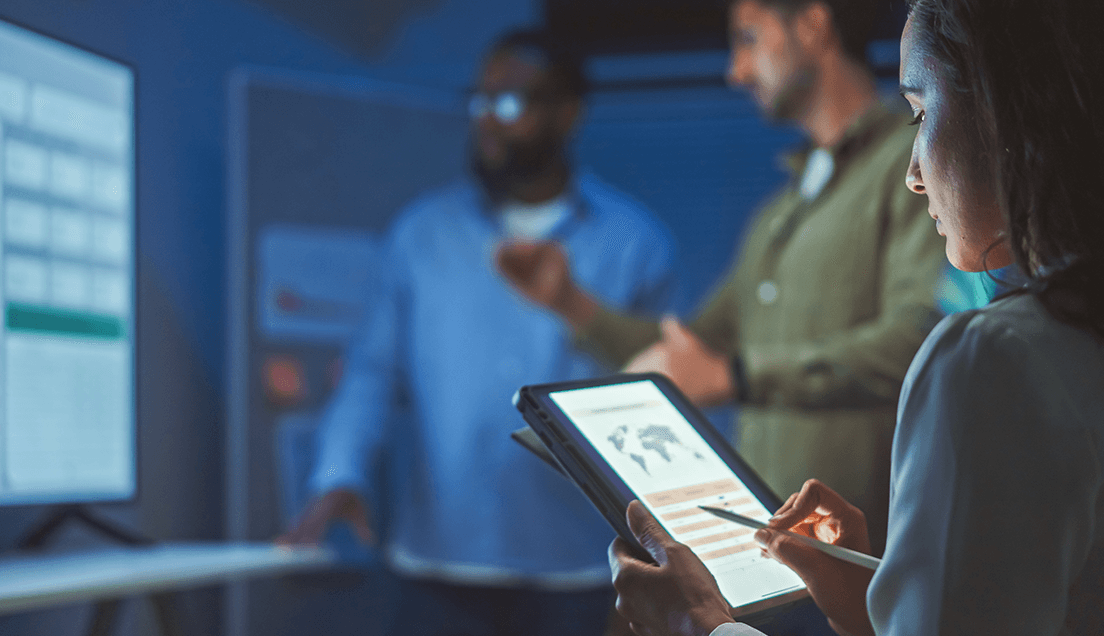 People In a Dark Office Looking at a Monitors and a Tablet