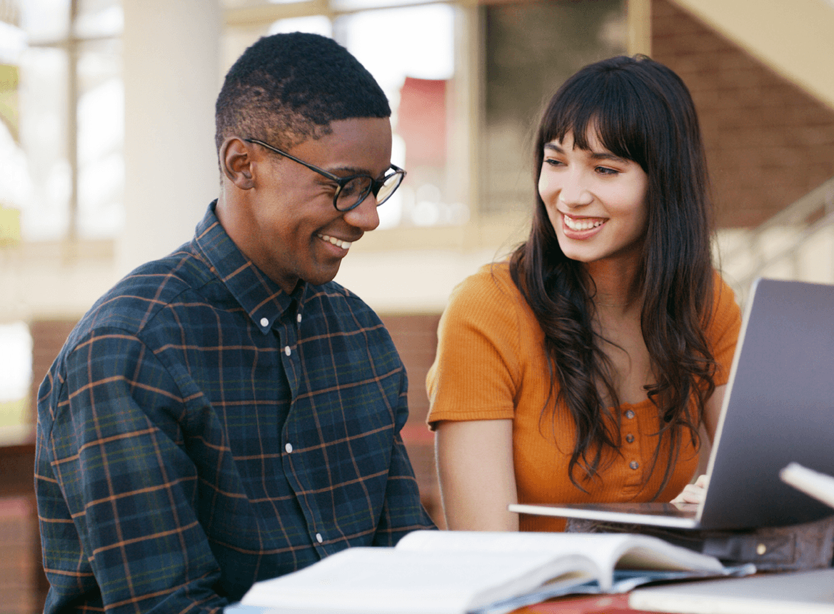Two People Smiling While Surrounded by Books and a Laptop